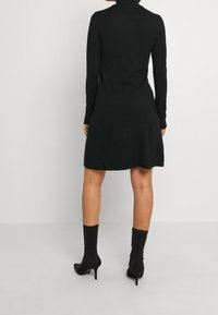 Svart långärmad klänning med polo hals, som slutar försiktigt vid midjan. Bärs med svarta ankellånga stövlar och ribbade strumpor.