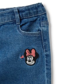 Vaqueros de mezclilla en azul medio con un bolsillo frontal y un diseño bordado de Minnie Mouse que presenta un lazo rosa y un acento de corazón.