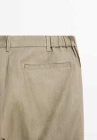Pantalon beige avec une taille élastique et une poche passepoilée arrière unique, présenté de dos sur fond blanc.
