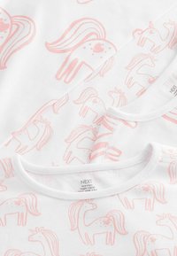 Tissu en coton blanc avec un motif de licornes roses répété, avec un col rond et des bretelles blanches. Étiquettes visibles au bas.