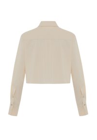 Afgekorte beige jas met een gestructureerde kraag, lange mouwen en knoopmanchetten. Gladde textuur en minimalistisch ontwerp met details aan de achternaad.