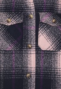 Ternet uldstof med nuancer af sort, pink og lilla, med brune knapper og to klaplommer.