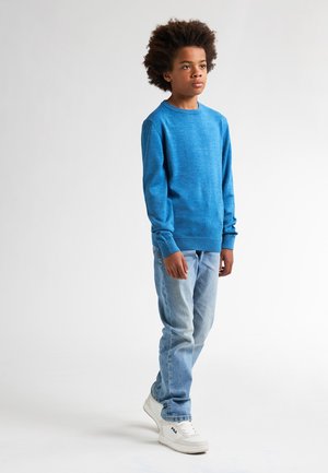 Pull en tricot bleu avec un col rond, associé à un jean bleu clair et des baskets blanches. Le pull a des manches longues et une finition texturée.