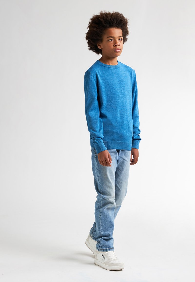 Maglione blu lavorato a maglia con collo rotondo, abbinato a jeans azzurri chiari e sneakers bianche. Il maglione ha maniche lunghe e una finitura testurizzata.