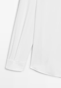 Biała koszula z długim rękawem, z mankietami i plisowanymi detalami na rękawie, wykonana z gładkiego materiału o delikatnym połysku.