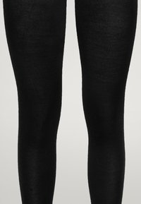 Svarta stickade leggings med en slät textur, figurnära stil och jämn färg, som sträcker sig från midjan till anklarna utan synliga sömmar.