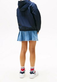 Námořnický modrý bunda s kapucí a elastickým lemem spárovaná s džínovou plisovanou sukní. Bílé tenisky s červenými a modrými pruhovanými ponožkami.