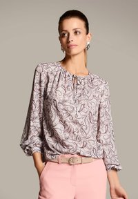 Langärmlige Bluse aus leichtem Material mit Paisleymuster, gerafftem Ausschnitt mit Kordelzug und lockerer Passform. Getragen mit hellrosa Hosen.
