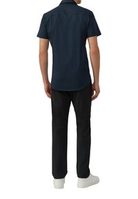 Navyblaues kurzärmeliges Hemd mit geradem Saum, glatter Textur und klassischem Kragen, kombiniert mit schwarzen Hosen und weißen Sneakers.
