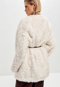 Faux fur-frakke i cremefarvet, med en struktureret, håret overflade, beltestrop til formning, og en tætsiddende silhuet.