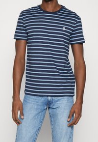Navy and light blue striped short-sleeve t-shirt, round neckline, featuring a small embroidered logo on the chest. Soft cotton fabric.