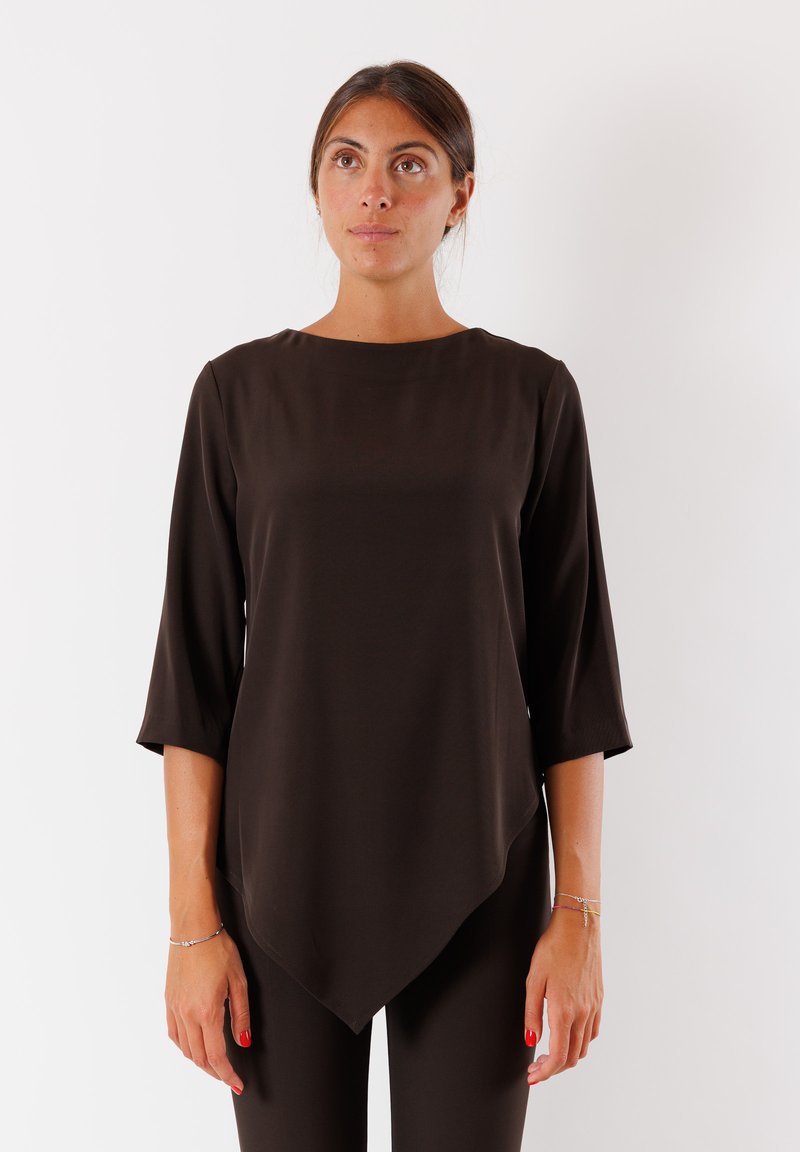 Top asimmetrico marrone con maniche 3/4, tessuto liscio, scollo rotondo e orlo obliquo. Indossato con un pantalone coordinato.