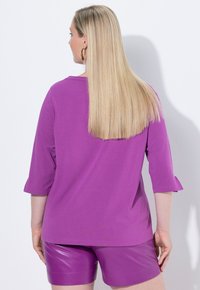 Paarse katoenen shirt met driekwart mouwen, voorzien van een ronde halslijn en een relaxte pasvorm, gecombineerd met glanzende paarse neplederen shorts.