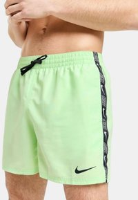 Pantaloni da bagno verde chiaro con cintura elastica, laccio nero e logo Nike. Presentano una striscia laterale nera con branding ripetuto.
