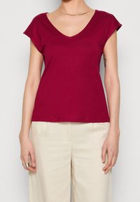 Burgundy short-sleeve V-neck t-shirt in soft fabric, featuring a straight hem and a relaxed fit, paired with cream-colored wide-leg pants.