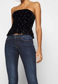 Svart sammetslinne utan axelband med röd blommig broderi, utsvängd nederdel, kombinerat med mörkblå tajta jeans. Slät yta, definierad form.