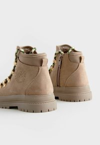Stivali alla caviglia in suede beige con lacci a motivo verde e nero, occhielli dorati e zip laterale. Suola in gomma spessa con battistrada testurizzato.