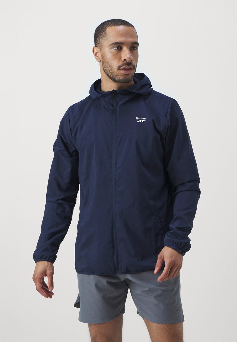 Mazu, vieglu jacci ar kapuci, pilna apkakle un elastīgām piedurknēm. Uz krūts uzšūta Reebok logo un tai ir brīvs griezums.