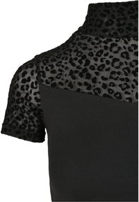 Svart topp med korte ermer som har et gjennomsiktig leopardmønster på skuldrene, med en tettsittende kropp i solid svart. Jevn tekstur generelt.