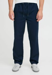 Marineblauwe broek van een gladde stof, met een elastische tailleband met trekkoord en zijzakken. Gecombineerd met lichtgrijze sneakers.