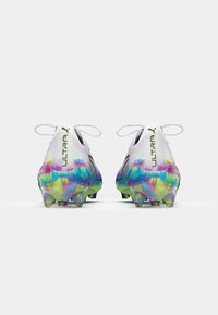 Puma Ultra soccer cleats featuring a white upper, vibrant tie-dye outsole, and prominent lacing system with green branding.