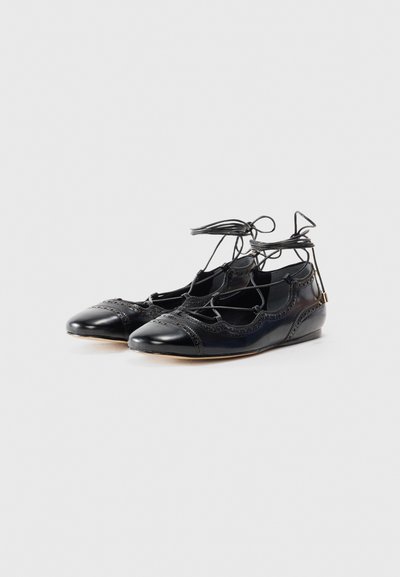 Black patent leather flats with a lace-up design, featuring decorative perforations and a rounded toe. Low wedge heel.