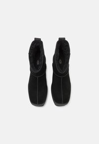 Zwarte suède enkelboots met een zachte voering van bont, voorzien van een trekband en contrasterende stiksels, stevige rubberen zolen.