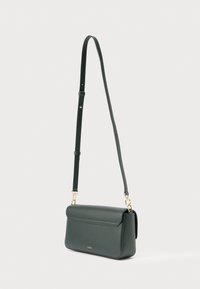 Tumši zaļa ādas plecu soma ar plakanu dizainu, zelta tonētas detaļas, regulējamu siksnu un minimālistisku estētiku.