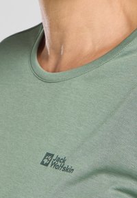 Kurzärmliges grünes T-Shirt aus weichem Stoff mit Rundhalsausschnitt. Verfügt über ein bedrucktes Logo in Dunkelblau im linken Brustbereich.