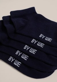 Jūras zilas kokvilnas zeķes ar baltu "BY WE" tekstu. Īsas, ribotas aproces, gluda tekstūra un viendabīga taisnstūra forma.
