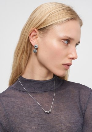 Silver-colored earrings feature two spherical elements, with a smooth metallic finish. A matching silver necklace has three smaller spheres.