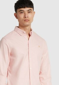 Camicia button-up rosa chiaro con colletto casual, caratterizzata da un piccolo logo ricamato sul petto e un tessuto liscio e testurizzato.