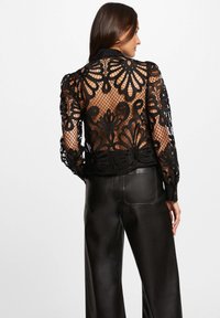 Camicia nera in pizzo con motivi floreali e schiena trasparente, caratterizzata da maniche lunghe e colletto, abbinata a pantaloni in pelle nera a vita alta.