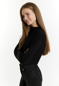 Maglione nero lavorato a maglia con colletto a costine, abbinato a jeans neri a vita alta, esposto su uno sfondo bianco uniforme.