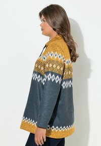 Maglione con motivo geometrico in giallo senape, grigio e bianco. Il suo design include un colletto e maniche lunghe, realizzato in tessuto testurizzato.