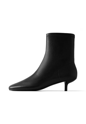 Bottine noire en cuir à bout pointu et petit talon kitten sur fond blanc, vue de profil.