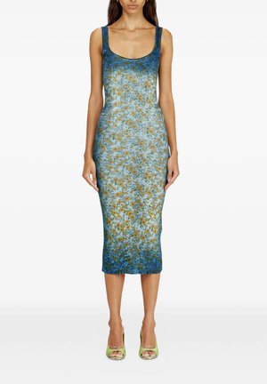 Donna che indossa un vestito midi floreale blu e verde senza maniche con trama a coste e scarpe verdi aperte in punta con tacco alto, in piedi davanti a uno sfondo bianco.
