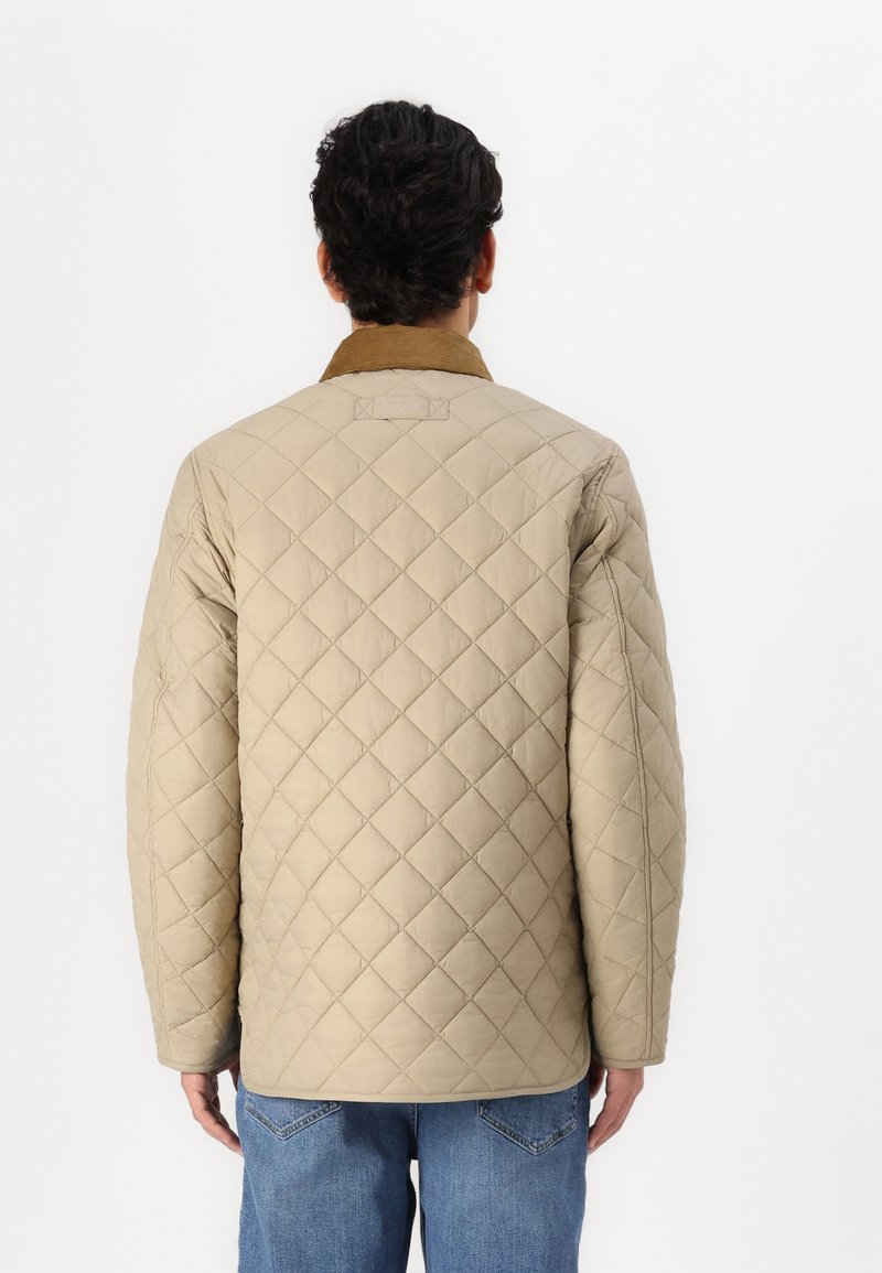 Beige gesteppte Jacke mit braunem Kragen, im Rautenmuster und mit Seitentaschen, kombiniert mit blauen Jeans.