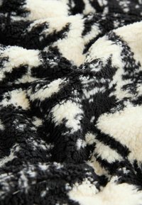 Schwarz-weiß gemusterte Plüschdecke mit einer weichen, strukturierten Oberfläche, die sich dick und flauschig anfühlt, und einem abstrakten Design.