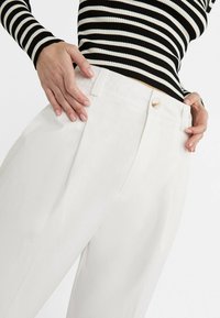 Pantalon blanc à jambes larges avec une texture lisse, doté d'une fermeture par bouton et de poches latérales, assorti à un haut rayé noir et blanc.