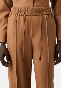 Bruine, zachte stofbroek met een tailleband met trekkoord, plooien en zilverkleurige hardware accenten. Gladde textuur en getailleerde pasvorm.