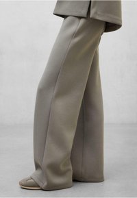Pantaloni a gamba larga e vita alta in morbido tessuto grigio, con una texture liscia e linee pulite, abbinati a calzature minimaliste.