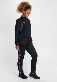 Schwarz sportliches Outfit mit einem Reißverschluss-Oberteil mit grauen Akzenten und schwarzen Hosen mit einem Fischgrätenmuster an der Seite. Strukturierten Stoff.