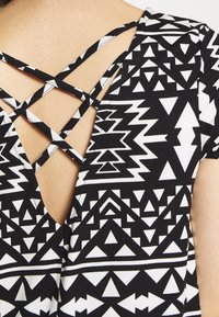 Haut à motif noir et blanc avec un design de bretelles croisées au dos, orné de formes triangulaires et géométriques sur le tissu.