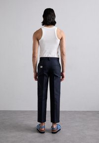 Granatowe, dopasowane spodnie fasonem slim z tylnymi kieszeniami, zestawione z białym, prążkowanym topem na ramiączkach i niebieskimi sandałami z brązowymi akcentami.