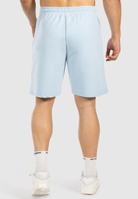 Pantalones cortos deportivos de color azul claro con una cintura elástica, textura suave, diseño de longitud hasta la rodilla y sin bolsillos visibles. Llevados con zapatillas blancas.