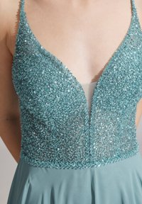 Abito blu senza maniche con scollatura a V profonda, ricoperto di paillettes scintillanti e gonna in tessuto liscio, indossato da una persona.