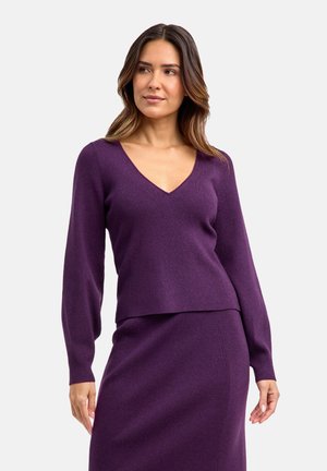 Lila gerippter Pullover mit V-Ausschnitt, langen Ärmeln und lockerer Passform, kombiniert mit einem passenden Rock. Glatte Textur und einheitliche Farbe.
