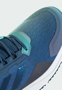 Modrá sportovní obuv s texturovaným textilním svrškem, síťkovým šněrováním a gumovou podrážkou. Obsahuje tyrkysové akcenty a elegantní design.