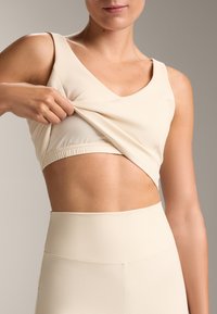 Hellbeige Sport-BH mit strukturiertem Muster, tiefem V-Ausschnitt und elastischem Saum, dazu eine passende strukturierte hochgeschnittene Hose.